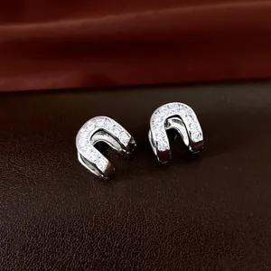 Detailed view of luxury zircon-studded oval hollow ear cuffs on a dark leather surface.