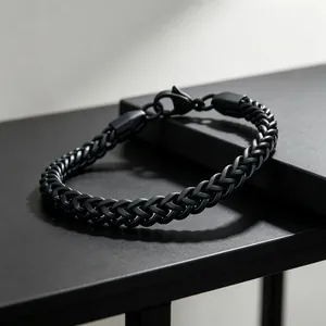 Close-up of matte black stainless steel wheat chain bracelet on minimalist stand