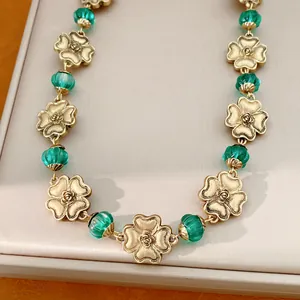 Nahaufnahme einer Vintage-Halskette mit goldenen Blüten und grünen Perlen