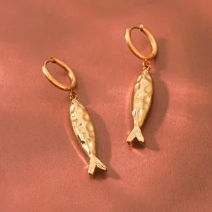 Gros plan de boucles d'oreilles poisson dorées avec une texture martelée unique