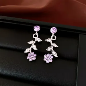 Nahaufnahme von Ohrringen mit lila Strassblumen und Blättern auf schwarzem Display.