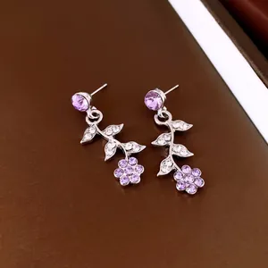 Nahaufnahme von silberfarbenen Ohrringen mit lila und klaren Kristallblumen und Blättern.