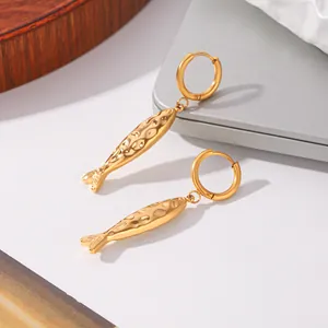 Détail en gros plan des pendentifs poissons dorés sur des créoles au style épuré