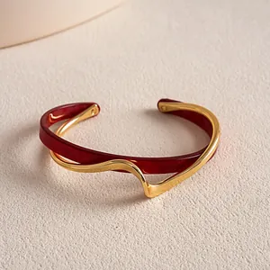 Nahaufnahme eines unregelmäßigen, wellenförmigen Armreifs aus Gold und rotem Acetat im Retro-Stil