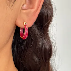 Detailansicht eines leuchtend rosa Emaille-Ohrrings am Ohr eines Models mit glänzendem Finish