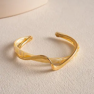 Detaillierte Nahaufnahme eines goldenen gewellten Armreifs mit marmoriertem Acetat-Inlay.