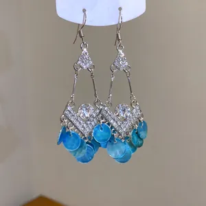 Detail van zilveren etnische hangoorbellen met blauwe schelpenkwastjes en strassteentjes