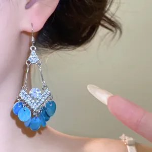 Detailopname van etnische oorbellen met strass en blauwe schelpenkwastjes op model.