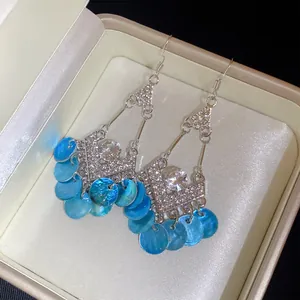 Close-up van strass ruitvormige oorbellen met blauwe schelpen franje in een doosje.