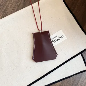 Detail van bordeauxrode lederen clochette ketting met wit stiksel en rood koordje.