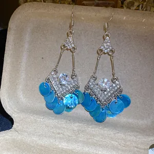 Detailopname van etnische oorbellen met blauwe schelpenkwastjes en ruitvormige strass