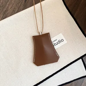 Close-up van een minimalistische bruine leren sleutelhanger ketting op wit textiel.