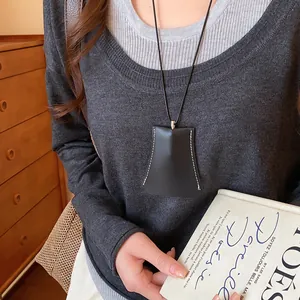 Close-up van een minimalistische zwarte lederen geometrische pouch ketting op een trui.