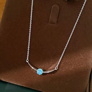 Minimalist curved silver necklace featuring a central round blue zircon on a dark velvet stand.