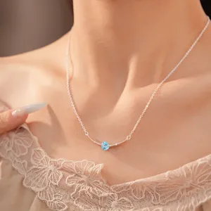Detailopname van een minimalistische zilveren ketting met een lichtblauwe zirkoon.