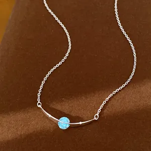 Detailopname van een zilveren gebogen halsketting met een briljante ronde blauwe steen