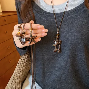 Vue détaillée des pendentifs ours et cœur à motif léopard sur un collier en cuir marron.