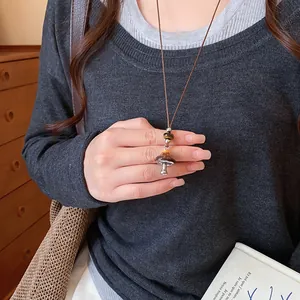 Détail d'un collier pendentif champignon avec émail léopard sur un cordon marron.