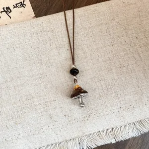 Gros plan détaillé d'un collier avec pendentif champignon marron sur un tissu beige texturé.