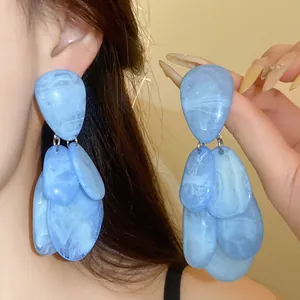Détail des boucles d'oreilles en résine bleu clair, portées et tenues à la main