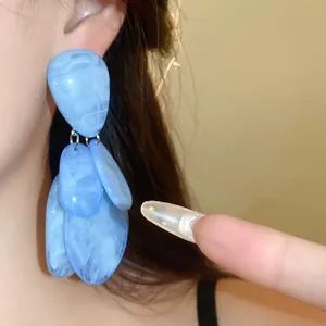 Gros plan de boucles d'oreilles pendantes en résine marbrée bleue sur une oreille.