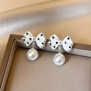 Close-up of elegant white polka dot bow earrings with dangling pearls on display.