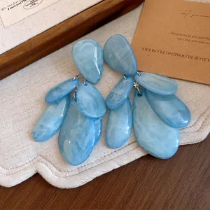 Détail de boucles d'oreilles pendantes en résine bleue avec texture marbrée.