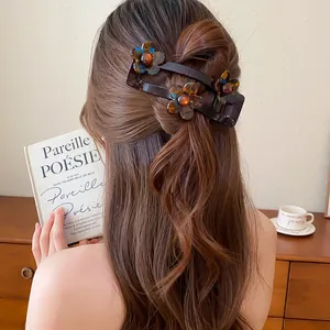 Détail d'une pince à cheveux fleur en acrylique marron chocolat portée sur de longs cheveux ondulés