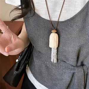 Elegante leren koordketting met witte parelkwastjes gedragen op een grijze gebreide top