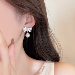Close-up detail of white polka dot bow earring with a dangling white pearl pendant.