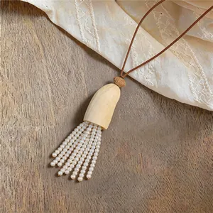 Detail einer eleganten Perlenquasten-Halskette mit braunem Lederband auf Holzoberfläche
