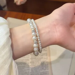 Nahaufnahme eines zweilagigen Perlenarmbands mit funkelnden Tonkugeln am Handgelenk.