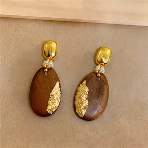 Detailansicht von ovalen Holzohrringen mit Goldfolie und kleinen weißen Perlen