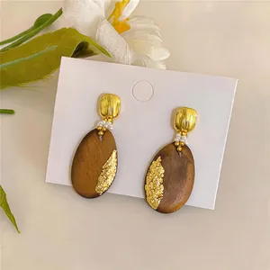 Nahaufnahme von ovalen Retro-Ohrsteckern aus Holz mit Goldfolie und Silbernadeln