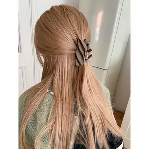 Achteraanzicht van een gestreepte mintblauwe en bruine haarklem van acetaat in blond haar