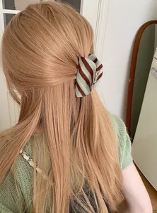 Detailweergave van een blauw-bruin gestreepte acetaat haarklem in blond haar van achteren