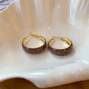 Boucles d'oreilles créoles émaillées marron à pois blancs dans une coupelle coquillage.