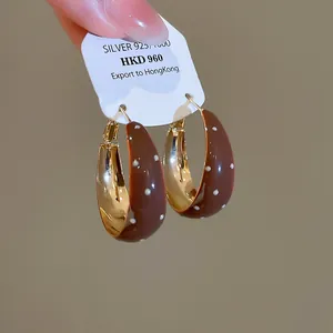 Vue détaillée de boucles d'oreilles créoles en émail marron à pois sur une carte