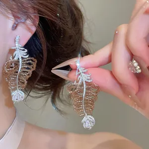 Gros plan sur ces boucles d'oreilles feuilles avec zircons étincelants et perles brunes.