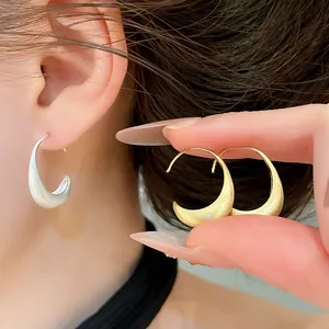 Close-up detail of minimalist brushed metal crescent earrings in silver and gold finishes