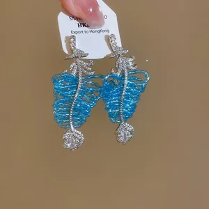 Détail de boucles d'oreilles feuille en zircon avec pompons bleus et pendentifs goutte
