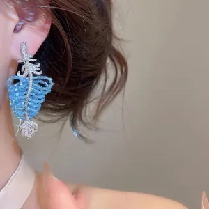 Détail élégant de boucles d'oreilles en feuilles perlées bleues avec zircons.