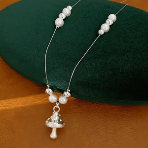 Detailansicht eines silbernen Pilzanhängers mit eleganten weißen Perlen und silbernen Perlen.