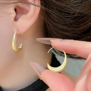 Close-up of brushed gold C-shaped earrings with matte finish on ear and hand