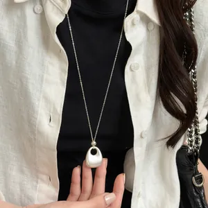Close-up van een Franse retro ketting met mat zilveren hanger op een wit linnen overhemd.