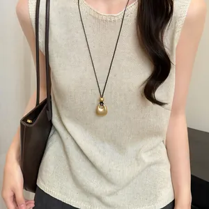 Detailopname van een Franse retro goudmetalen druppelvormige hangerketting op beige top