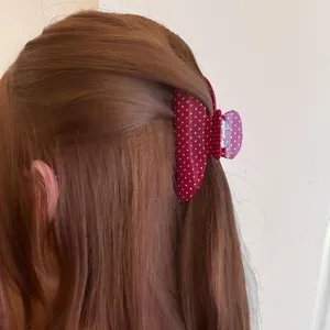 Close-up view of a stylish burgundy polka dot hair claw clip worn on reddish-brown hair