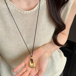 Detail van een vintage ketting met matgouden hanger gedragen op een beige gebreide top