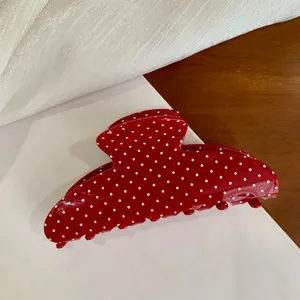 Macro detail of a large red hair claw clip featuring a classic white polka dot pattern design