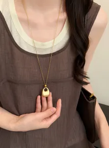 Gedetailleerd overzicht van een gouden ketting met druppelhanger op een bruine jurk